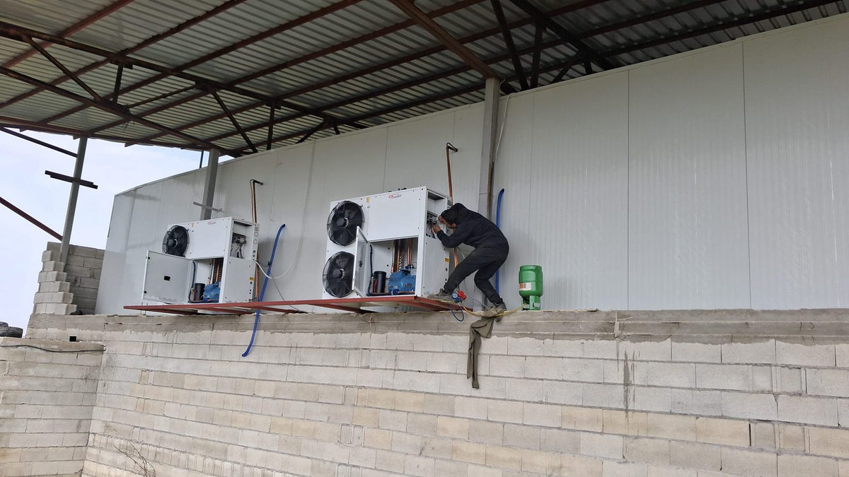 Teknisyen, duvara monte edilmiş iki kondenser ünitesinin bağlantılarını yapıyor